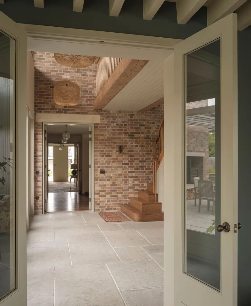 View through open doorway to entrance hall with stone floor tiles and brick walls under timber beams