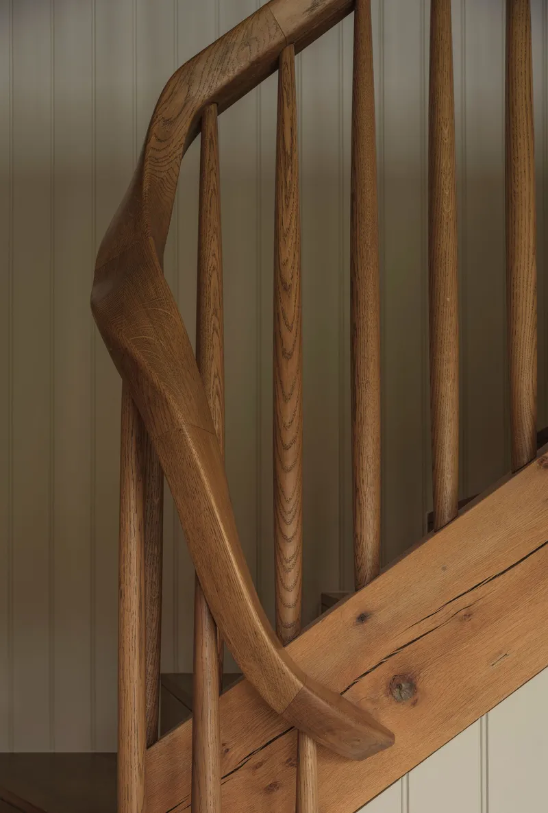 Close-up of curved oak handrail and vertical balusters against painted tongue-and-groove wall panels