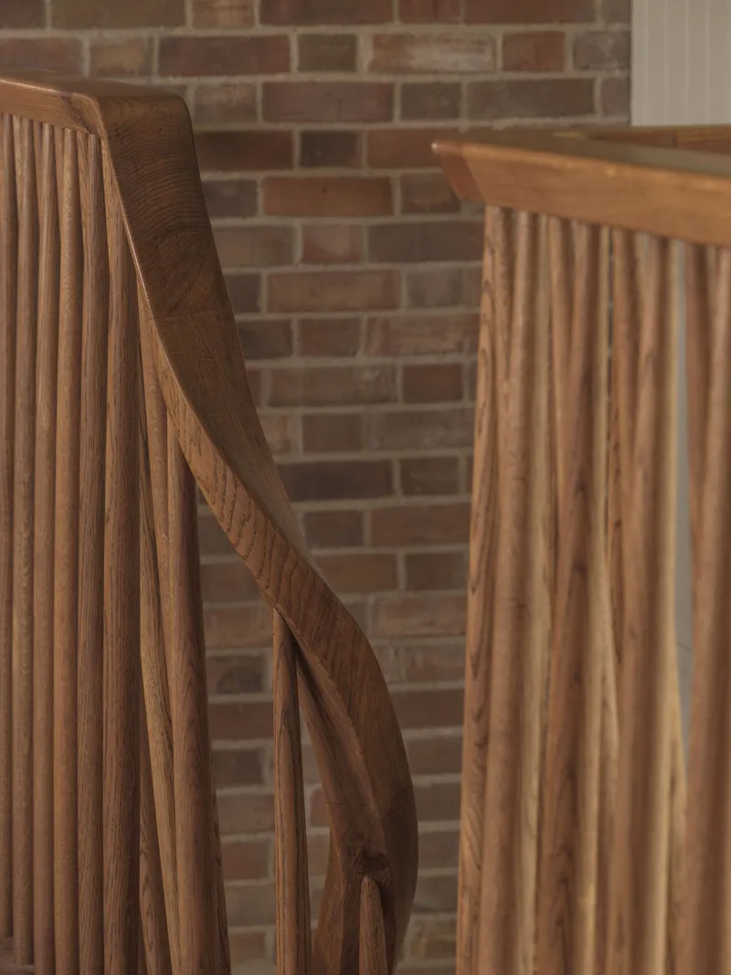 Oak staircase with curved handrail and vertical slats against an exposed brick wall