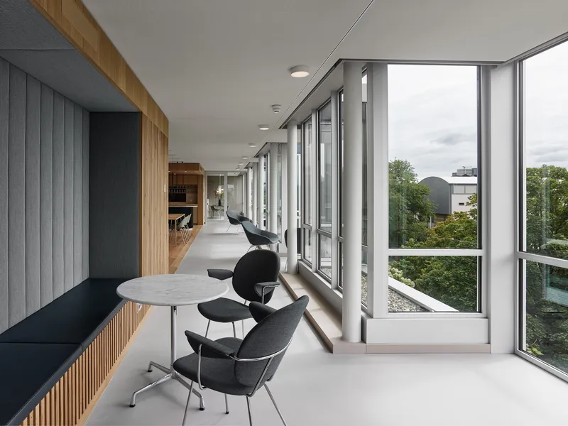 Corridor with floor-to-ceiling windows and black lounge seating overlooking treetops