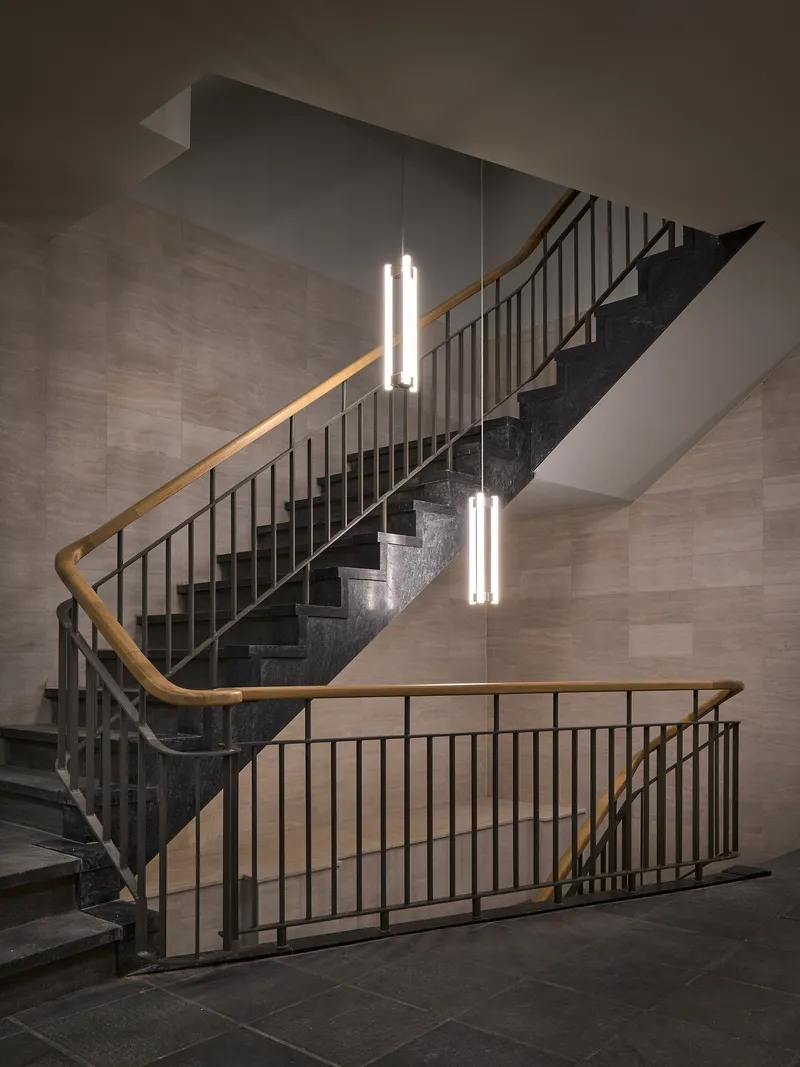Double-height staircase with dark terrazzo treads, metal railings and tubular pendant lights