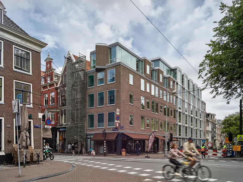 Street view of the mixed brick and glass facade with cyclists passing under cloudy skies