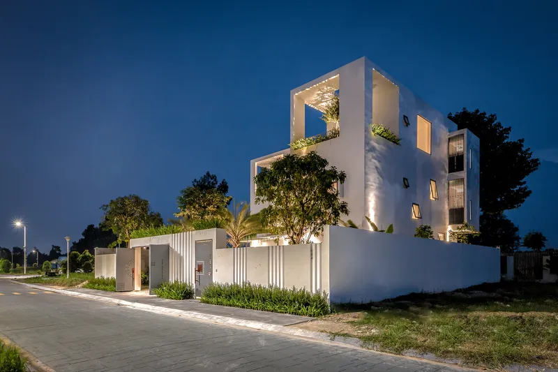 Corner view at twilight showing stacked white volumes with framed tree planters and uplighting