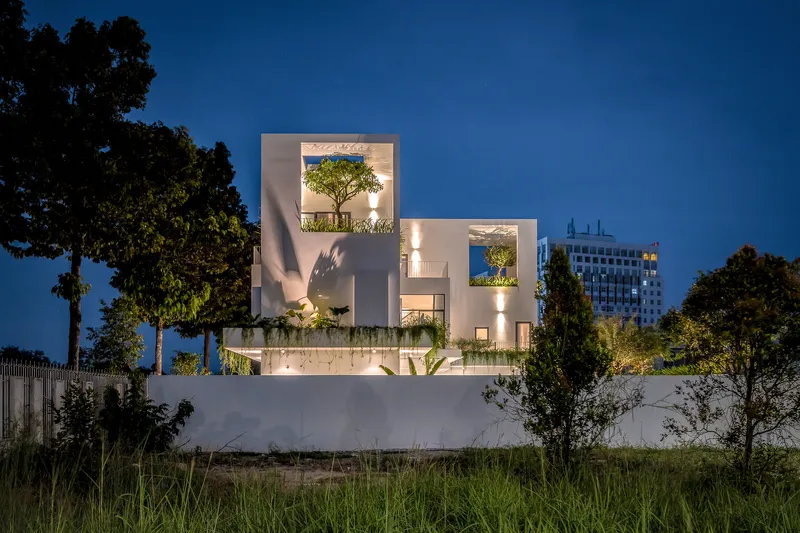 Rear elevation at dusk with illuminated terraces framing trees against the night sky