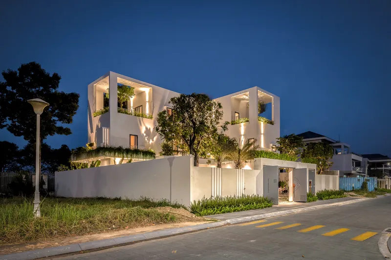 Street view of the white cubic volumes with planted terraces at twilight