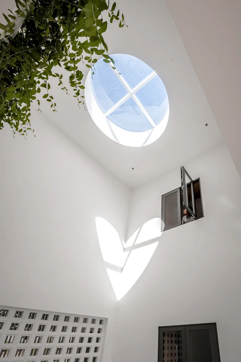 Double-height interior space with circular skylight casting geometric shadows on white walls