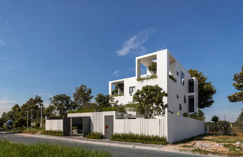 Corner view of the stepped white volumes with planted balconies and perimeter fence