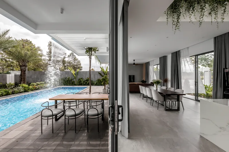 Open dining area with floor-to-ceiling glass doors connecting to a covered poolside terrace with slatted pergola