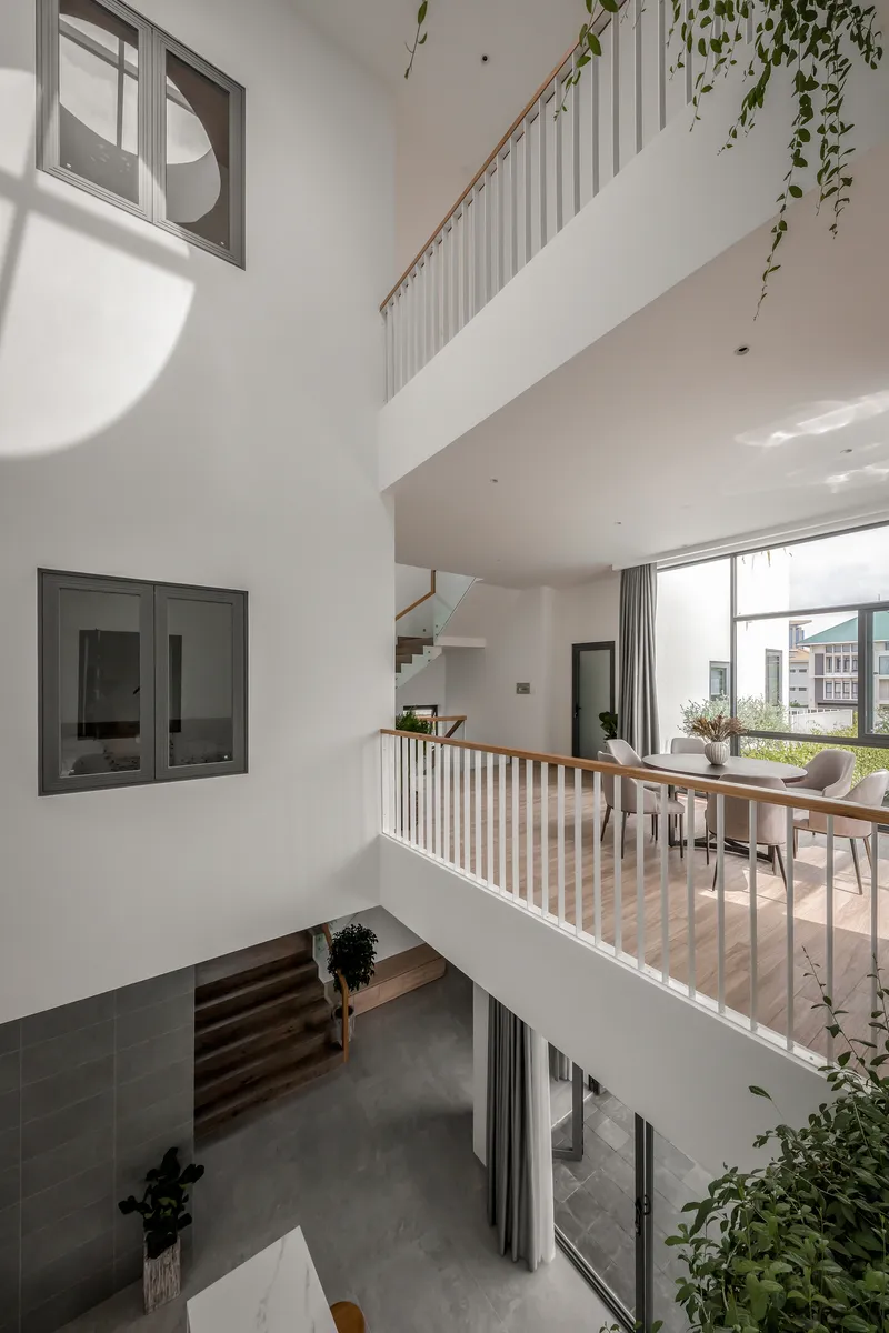 Triple-height void with timber-railed bridges linking levels and windows puncturing white walls in morning light