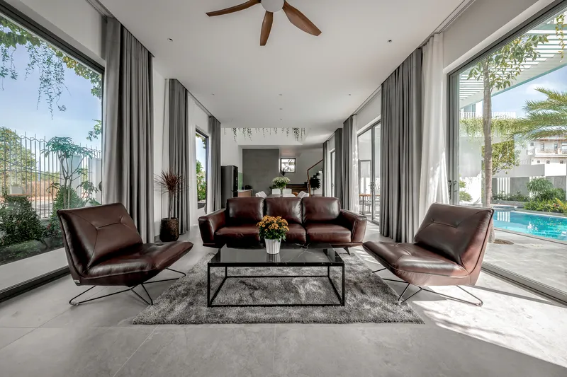 Living room with brown leather seating and full-height glass walls framing views to the garden and pool