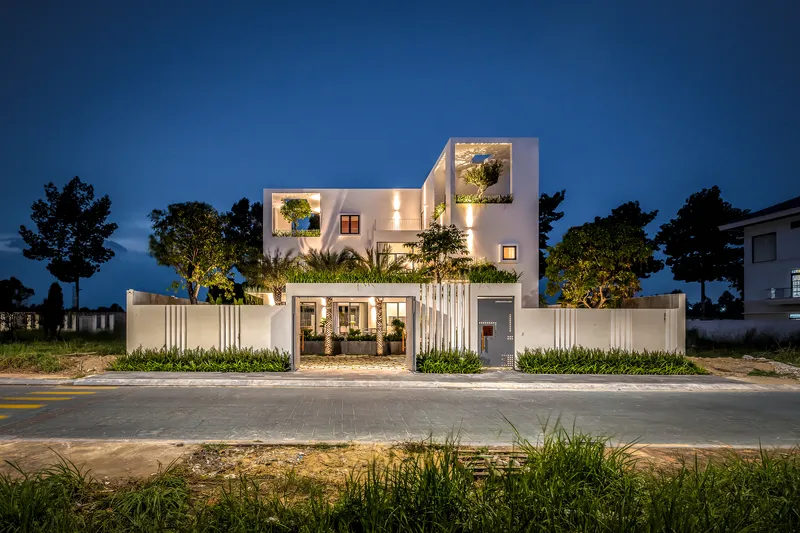 Front elevation at dusk with illuminated interior courtyard and planted perimeter wall