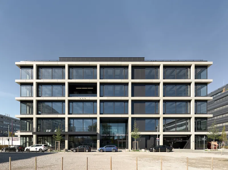 Street-facing facade with rhythmic white concrete frame and recessed dark glazing under a clear sky