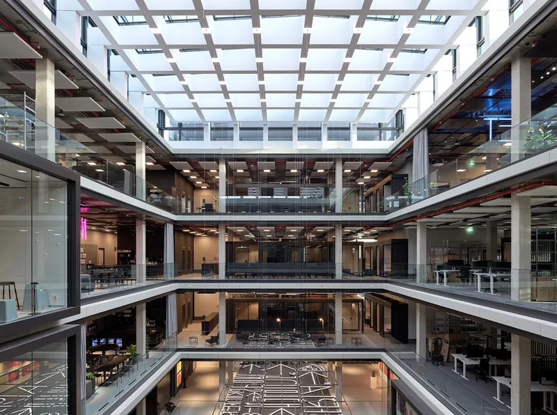 Central atrium looking up through four office levels toward a gridded glass roof structure