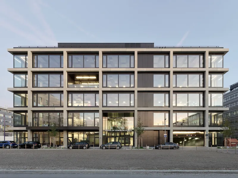 Street-facing facade with precast concrete grid framing floor-to-ceiling windows under an overcast sky