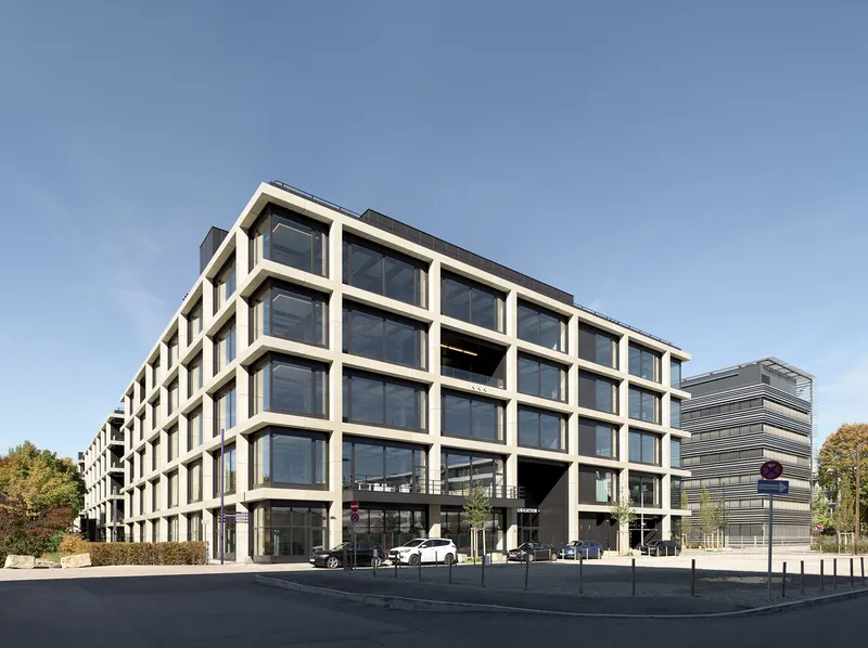 Corner view of the precast frame facade with ground-level entrance and bollards in afternoon light