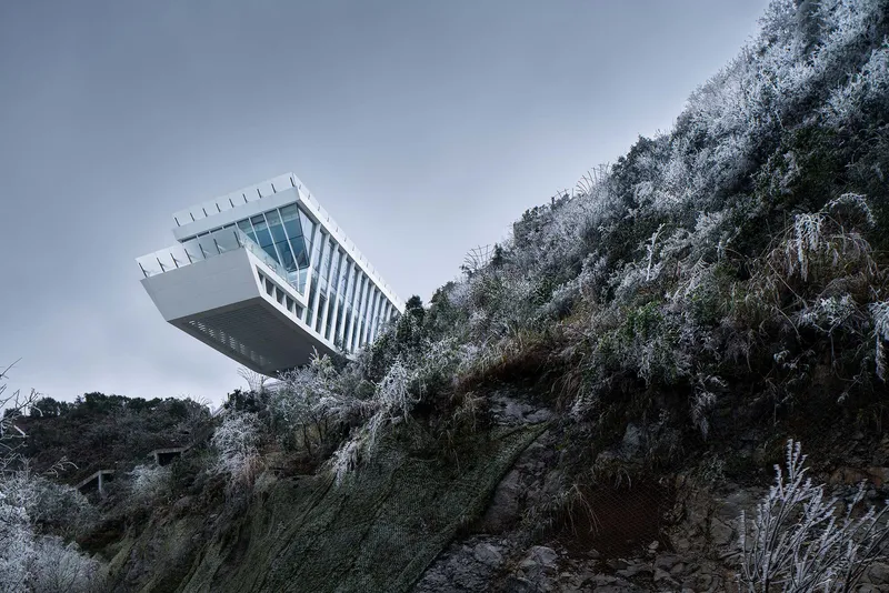 Side view of the white steel-framed cantilever projecting from the frost-covered cliff face