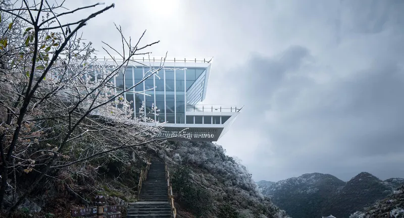 Glass enclosed viewing platform on rocky summit approached by stone steps with bare trees in winter