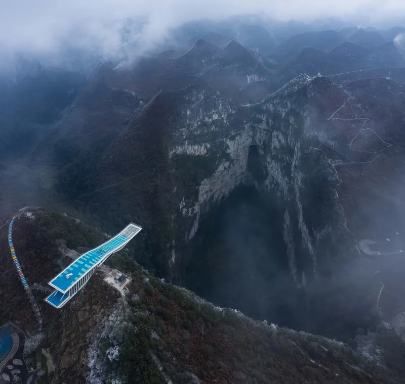 Aerial view of the cantilevered blue-roofed viewing platform extending over a misty mountain gorge