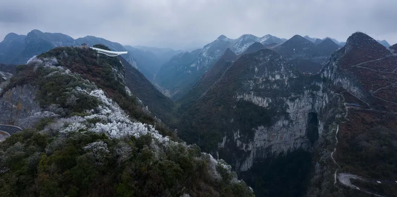 Distant view of the white cantilevered structure perched on a frosted ridgeline above steep valleys