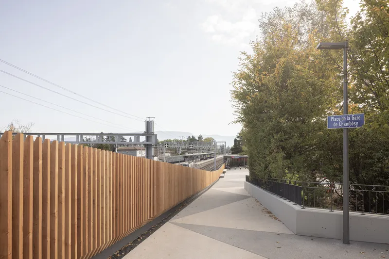Elevated pedestrian walkway with continuous vertical timber screening alongside a tree and railway infrastructure