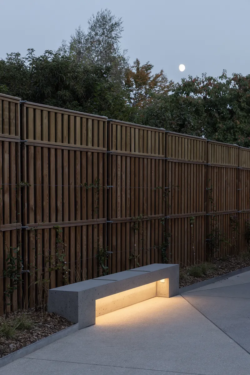 Vertical timber screen fence beside a concrete bench with integrated lighting at dusk under moonlight