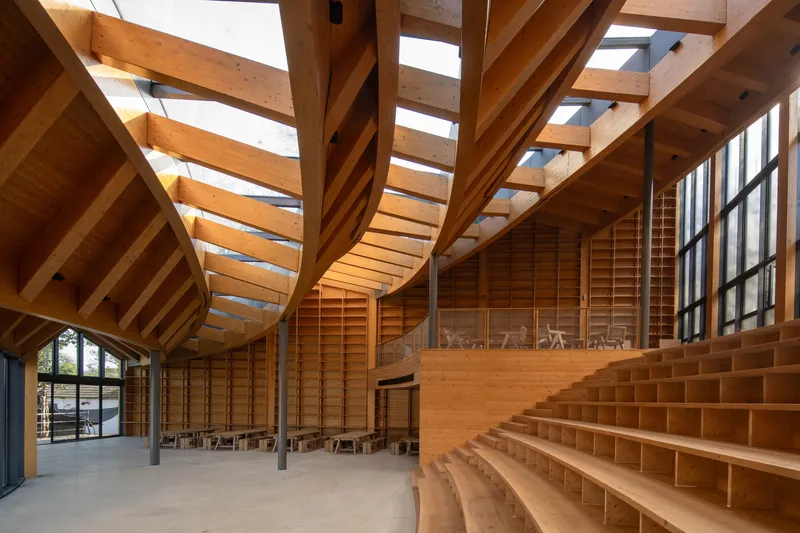 Interior timber hall with radiating glulam beams and stepped seating under clerestory glazing