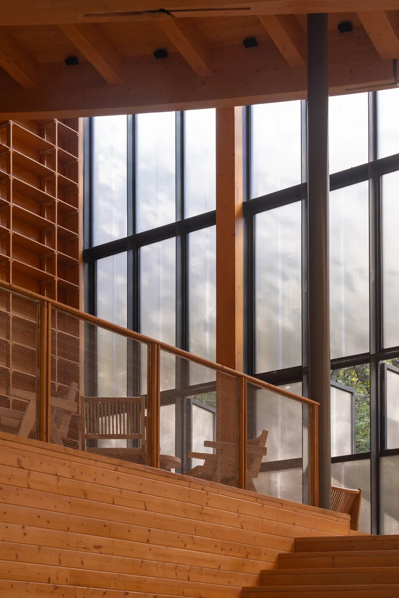 Upper level reading balcony with timber shelving and metal-framed windows overlooking the hall