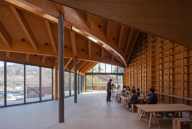 Reading room with timber shelving, curved roof structure, and visitors seated at tables beneath continuous glazing