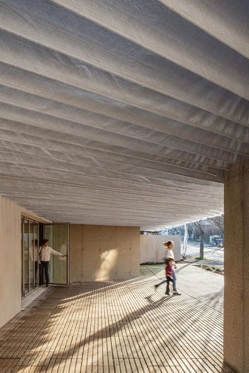Covered entrance with pleated metal ceiling and two figures in motion on tiled paving