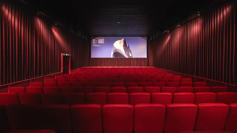 Auditorium view toward the screen with raked red seating and ribbed wall cladding