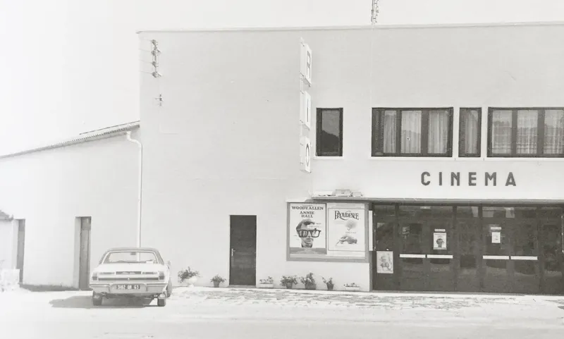 White stucco cinema facade with rectangular windows and a parked car in front
