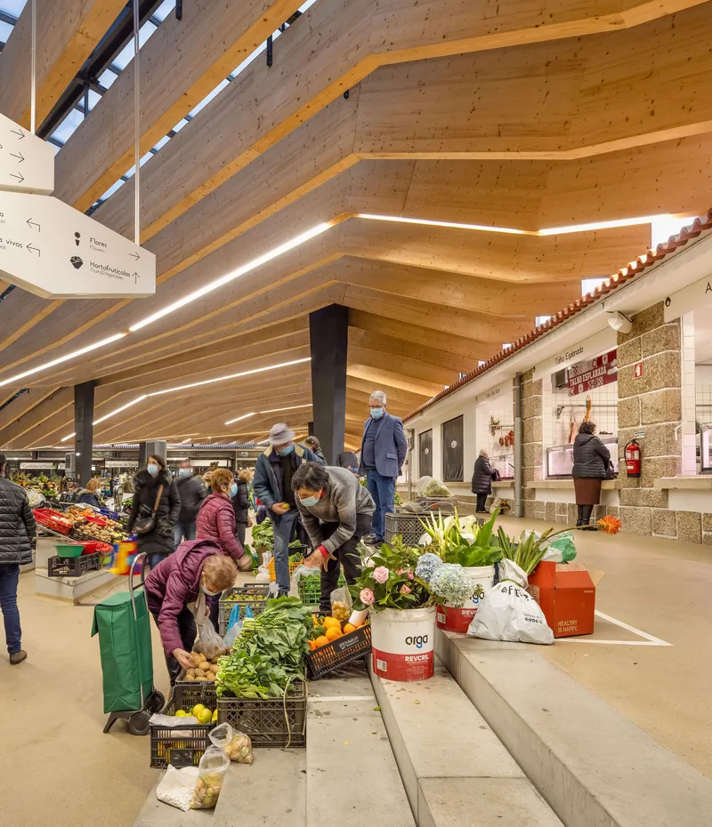 Market aisle with families shopping beneath the rippling timber beams and integrated linear lighting