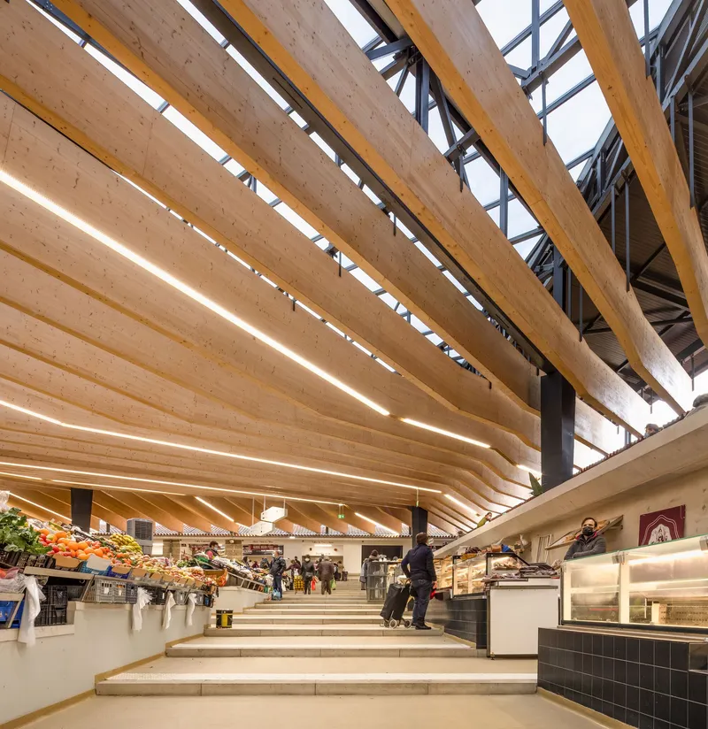 Wide concrete steps connecting market stalls under a sweeping laminated timber roof with exposed black steelwork