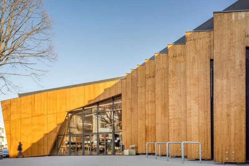 Oblique view of the timber-clad facade with vertical buttresses and glazed entry in afternoon light