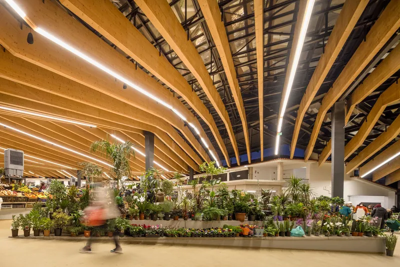 Interior market hall with curved laminated timber beams, integrated lighting strips, and plant displays below