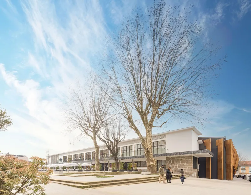 View across the stepped plaza with bare winter trees and a two-story facade with vertical wood cladding