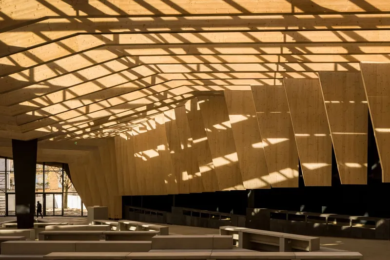 Interior showing timber acoustic wall panels with diagonal shadow patterns cast from glazed roof structure