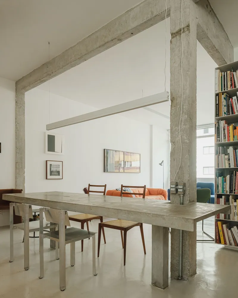 Concrete dining table wrapped by a structural column beside a floor-to-ceiling bookshelf