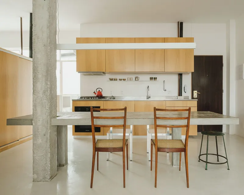 Kitchen with blonde wood cabinets viewed across the concrete dining table and structural column