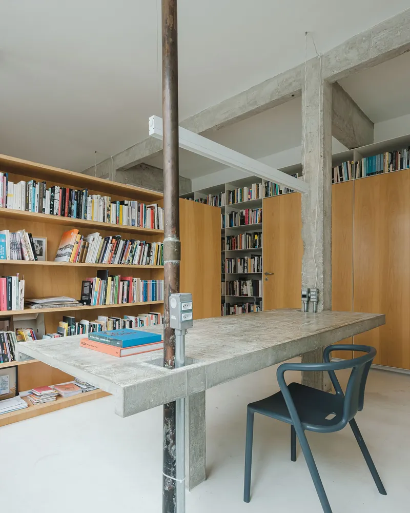 Library corner with blonde wood and built-in shelving flanking the concrete table and steel pipe