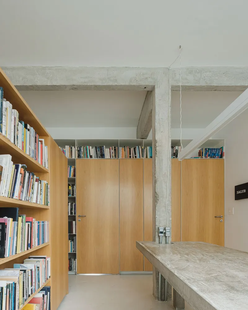 Exposed concrete beam spanning between columns above timber doors and built-in bookcases