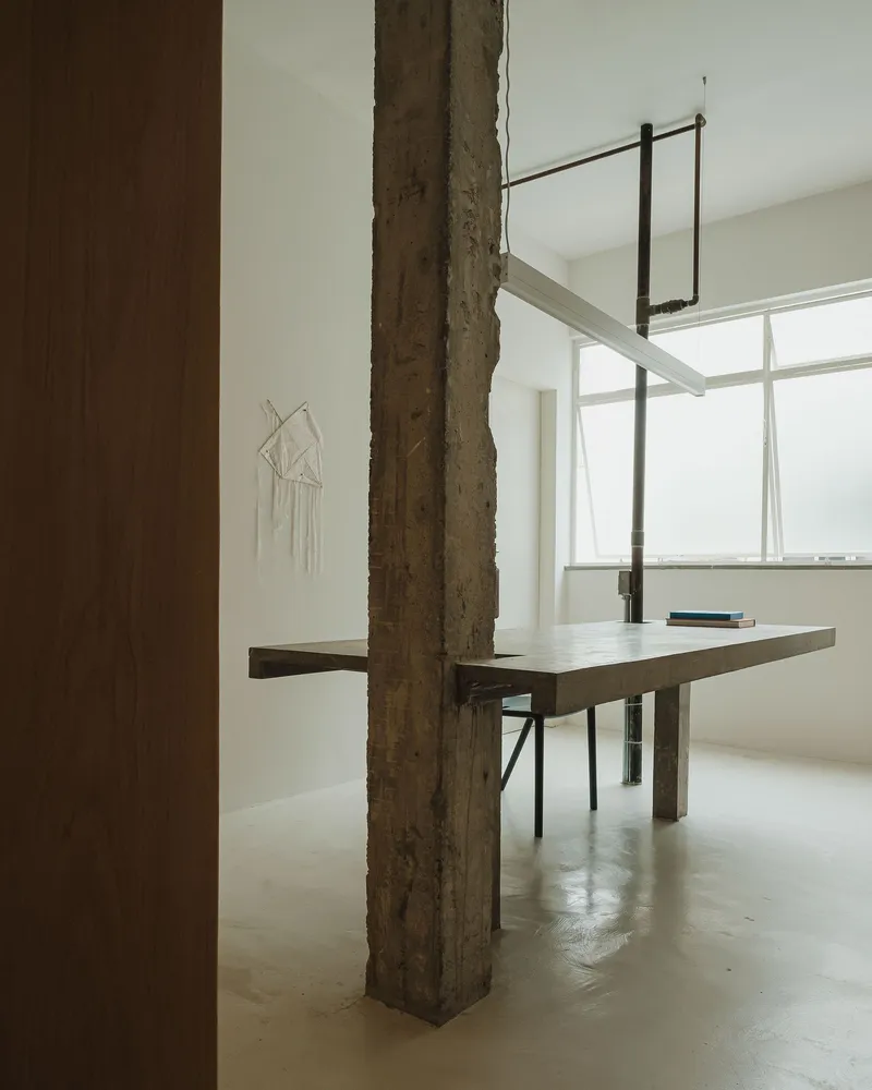 Concrete table integrated with a rough structural column beneath suspended lighting fixtures