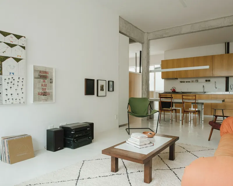 Open living area with exposed concrete beams and a kitchen beyond a patterned rug