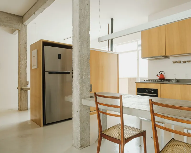 Kitchen with light wood cabinetry and concrete counter wrapping around a structural column