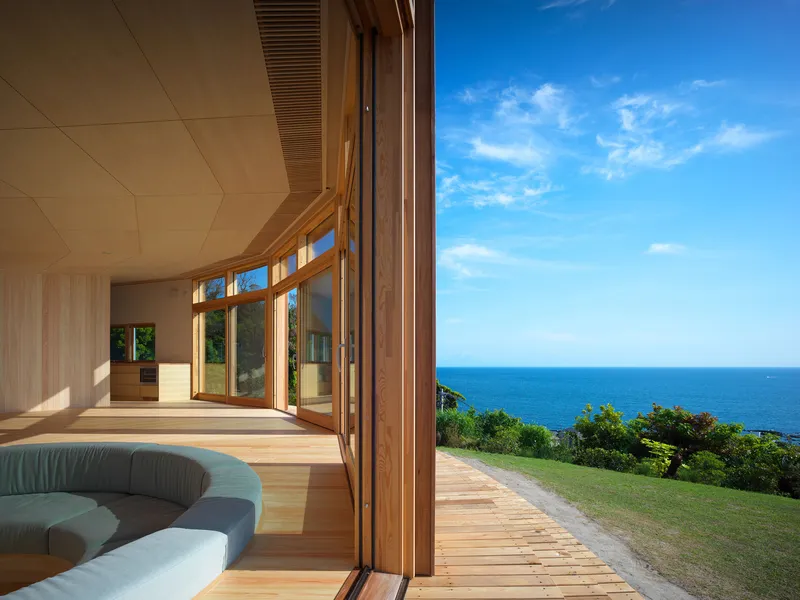 Open timber-framed doors leading to a coastal lawn with ocean view beyond