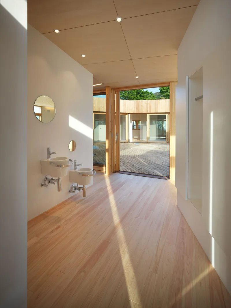 Corridor with wall-mounted sinks and view through timber doors to courtyard in sunlight