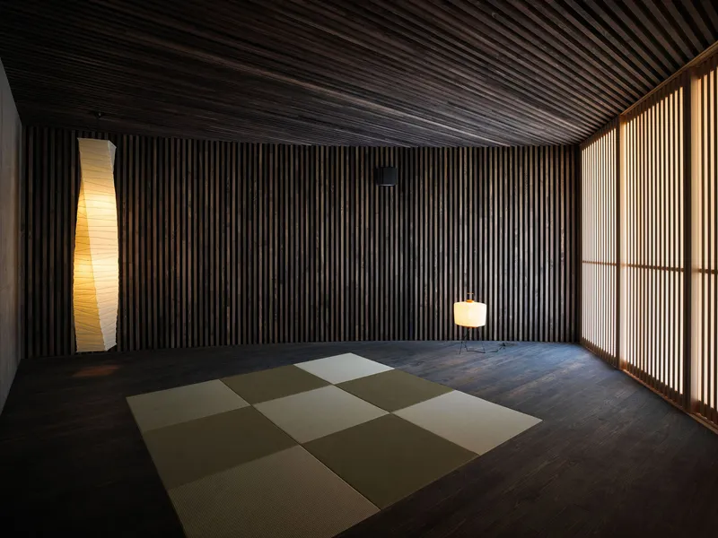 Interior room with vertical timber battens on walls and ceiling, backlit screen panels and chequered tatami mats on dark timber floor
