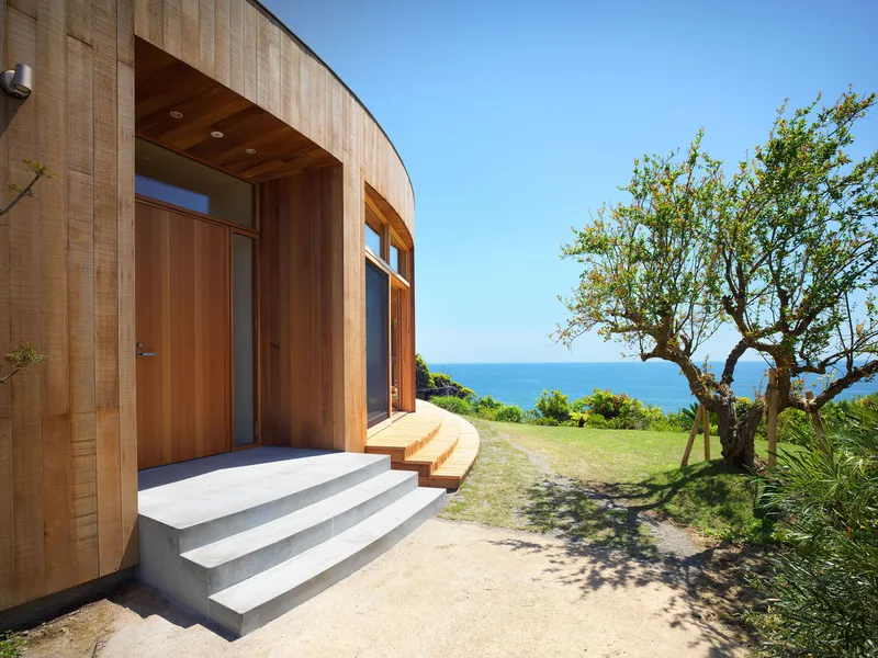 Entry with concrete steps and timber door under a curved soffit with ocean views beyond