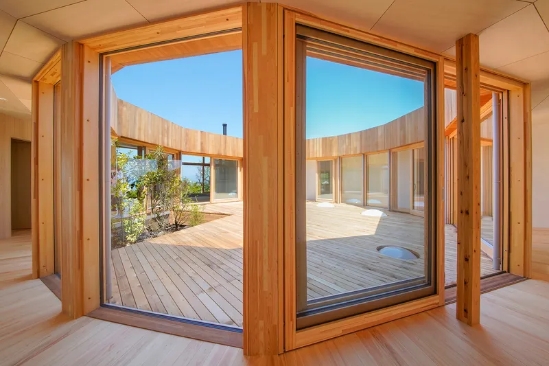 Open timber-framed glass doors revealing a central courtyard deck framed by the curved building wings