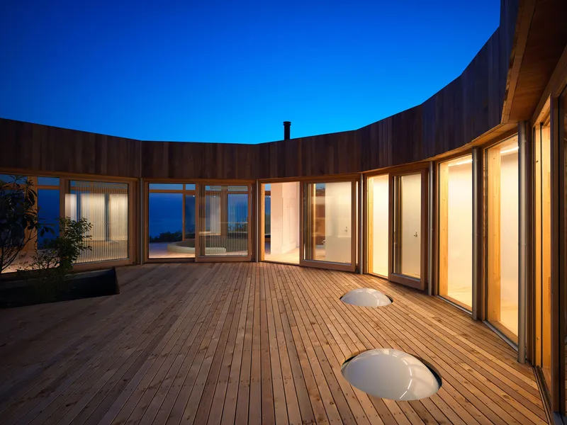 Timber courtyard deck with circular skylights and glazed facade at dusk under deep blue sky